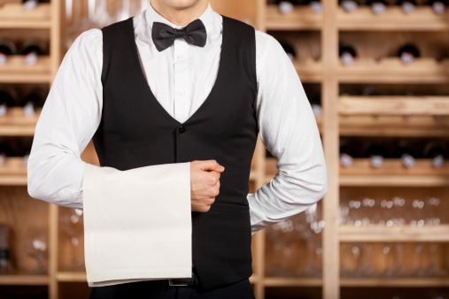 waiter in a vest and bowtie holding a restaurant napkin