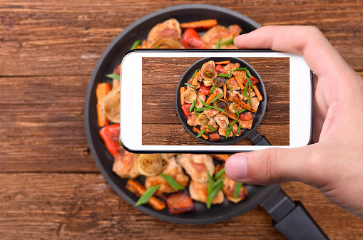 Hands taking photo of meat with vegetables with smartphone.