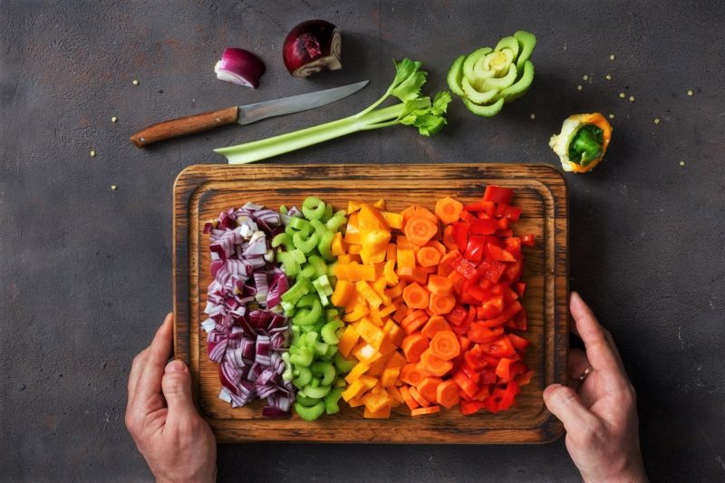 man holding cutting board with rainbow veggies