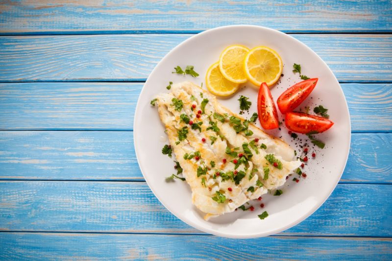 white fish on a plate with lemons and tomatoes
