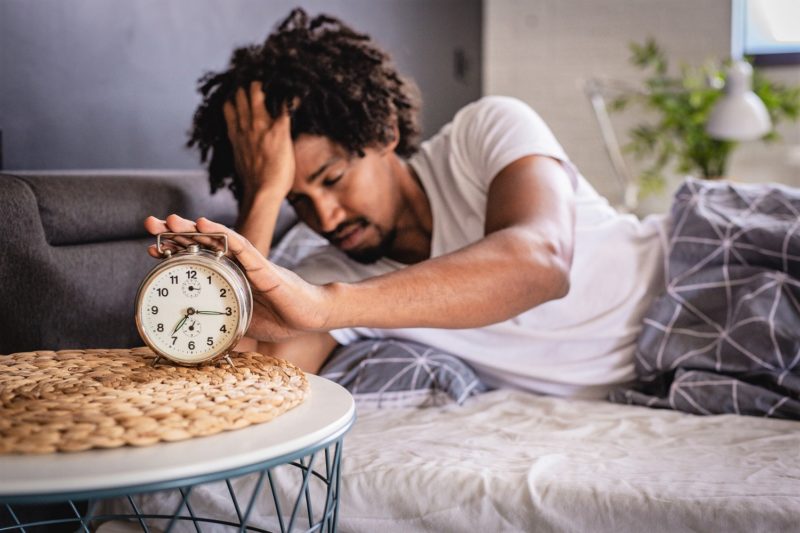 Man pressing the snooze button to get better sleep.
