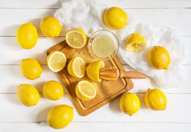 fresh lemons and a bowl of unlimited lemon juice on a cutting board with a handheld juicer