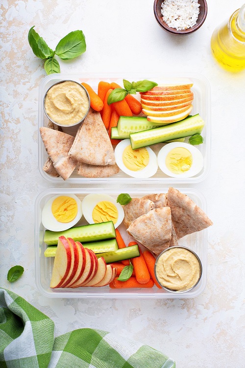 Healthy and nutritious snack boxes with veggies, pita bread, hummus, apple slices and a hard boiled egg