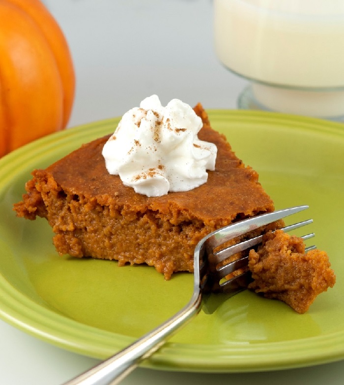 Fork cutting into a fresh slice of pumpkin pie topped with whipped cream