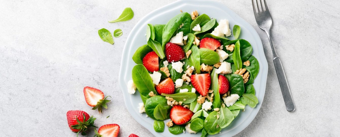A plate of spinach strawberry and walnut salad