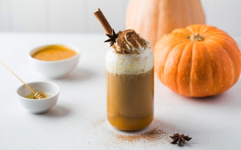 Pumpkin coffee with whipped cream and spices on table