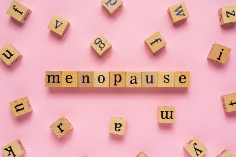 Menopause word on wooden block. Flat lay view on light pink background.
